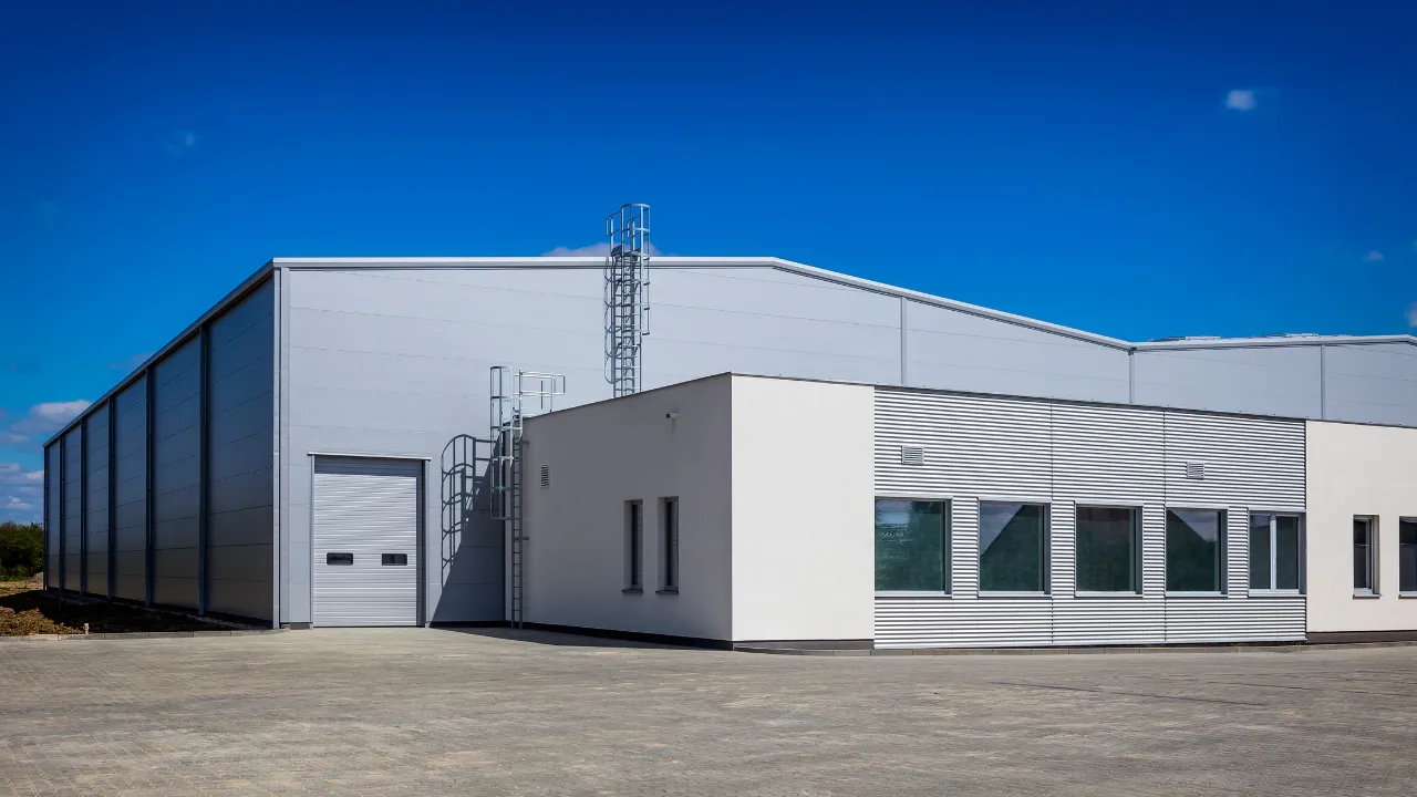 Modern industrial building with a white facade and attached offices, featuring large garage doors and exterior metal stairs, set against a clear blue sky.